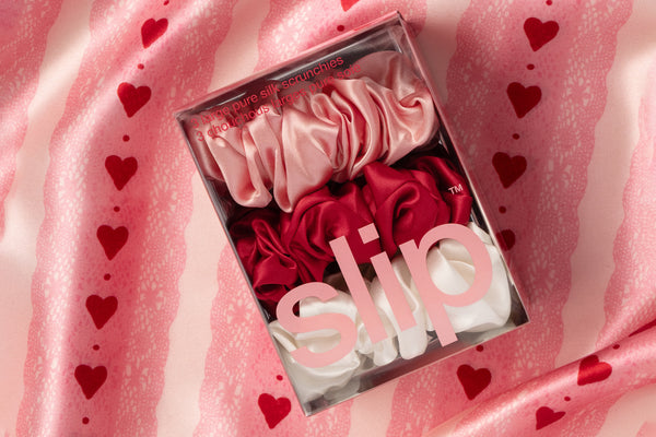 Set of white, pink and red scrunchies in a clear box on a pink fabric background with heart patterns.