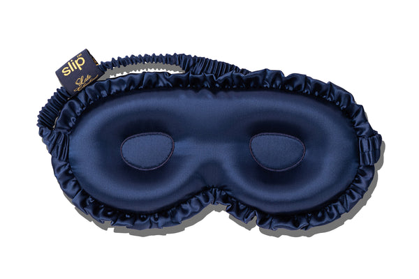 A navy blue silk sleep mask with a matching ruffled edge, featuring a small brand tag that reads 'slip' in gold lettering, set against a plain white background.