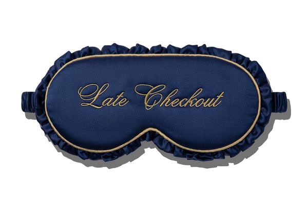 A navy blue frill silk sleep mask with gold embroidered trim and the words 'Late Checkout' in gold script on the front, shown on a white background with a soft drop shadow.