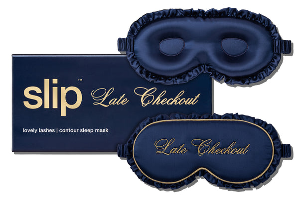 A navy blue frilled silk sleep mask with gold piping and 'Late Checkout' script, shown alongside its matching navy box with gold lettering. 