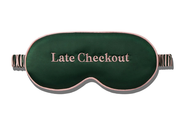 Green sleep mask with 'Late Checkout' embroidered in pink text on a white background