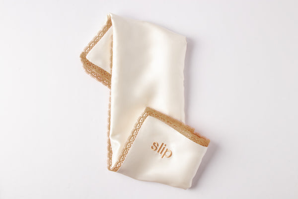 Folded white pillowcase with gold lace trim on a light gray background
